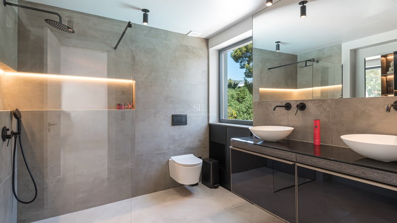 Salle de bains contemporaine avec grands carreaux gris, douche à l'italienne, double vasque et robinetterie noir mat.