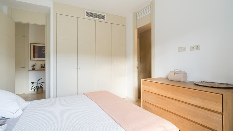 Chambre lumineuse avec placards crème, commode en bois et lit avec jeté de lit rose pastel.