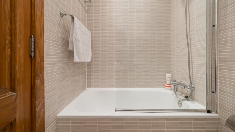 Baignoire blanche encastrée avec paroi vitrée et carrelage beige dans une salle de bain lumineuse.
