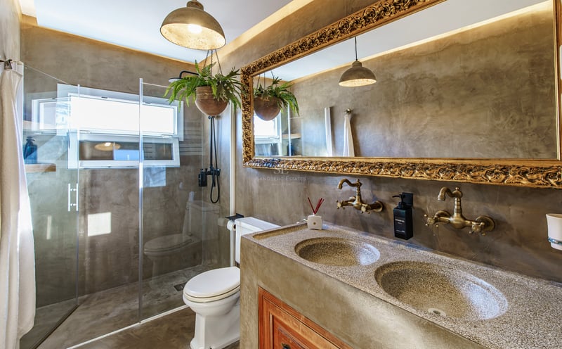 Salle de bain de luxe avec murs en béton, miroir doré orné, double vasque et douche en verre.