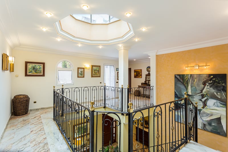 Palier avec sols en marbre, balustrade en fer forgé et verrière octogonale au plafond.