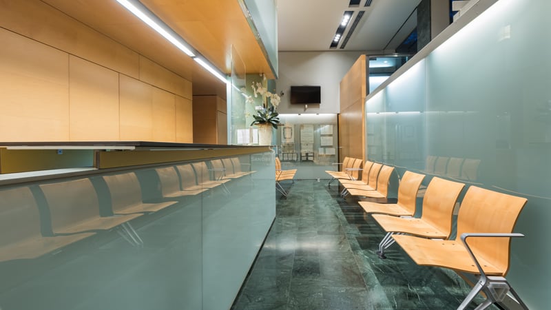 Modern reception area with frosted glass panels, light wood seating, and dark green marble flooring.