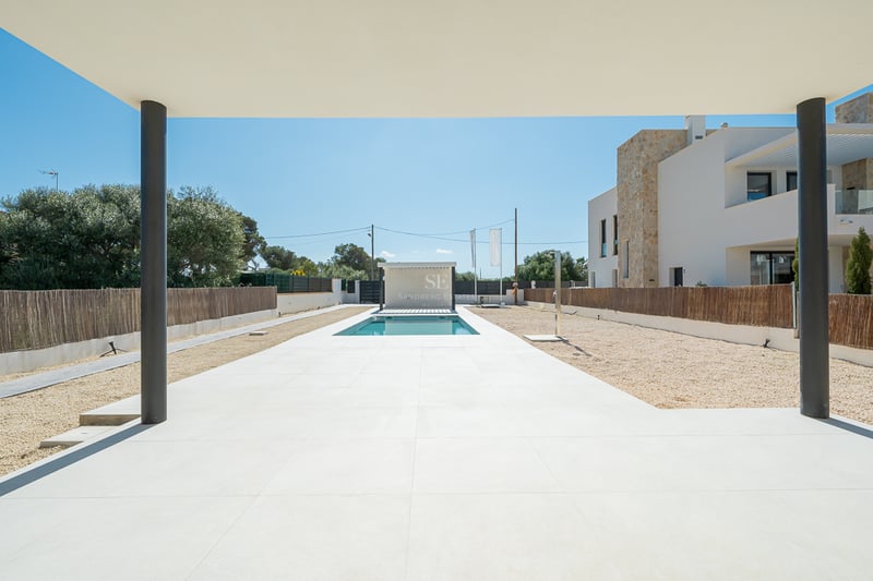 Vue depuis un porche couvert sur une piscine rectangulaire entourée de dalles blanches et de gravier dans une villa moderne.