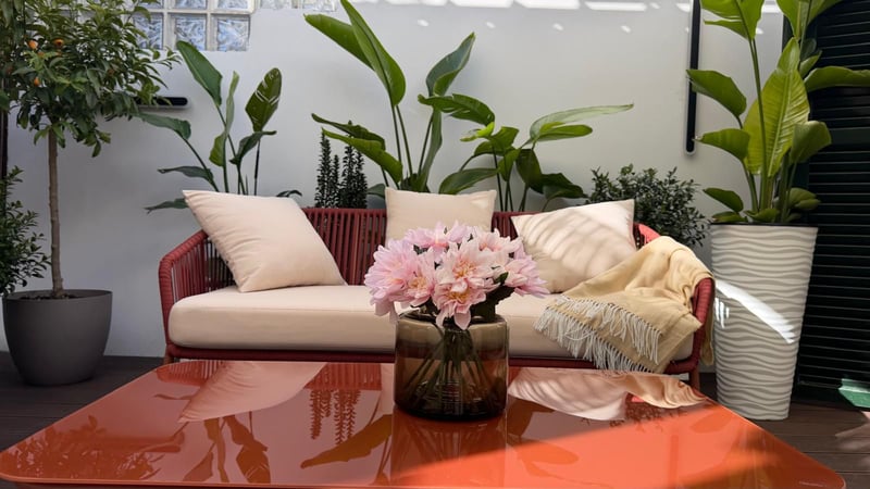 Canapé en corde rouge avec coussins crème sur une terrasse entourée de plantes tropicales et une table basse brillante.