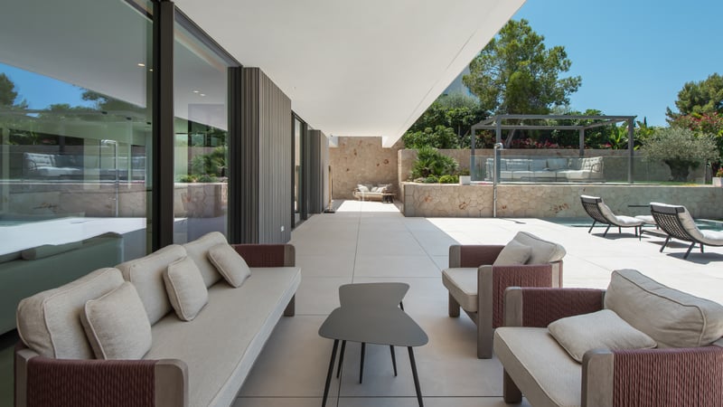 Vaste terrasse moderne avec mobilier de salon haut de gamme, murs en pierre et baies vitrées coulissantes.