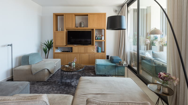 Salon lumineux avec canapés modulables en velours, table basse en marbre et baies vitrées ouvrant sur une terrasse.