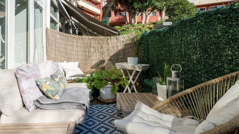 Terrasse ensoleillée avec canapé confortable, tapis géométrique et brise-vue en bambou dans un cadre côtier.