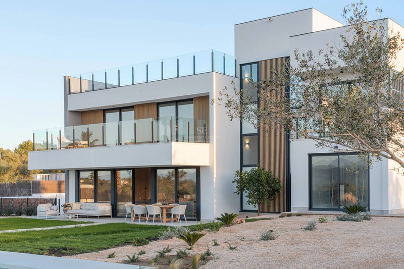 Zweistöckige moderne weiße Villa mit Glasbalkonen, Holzlamellen und Essbereich im Freien.