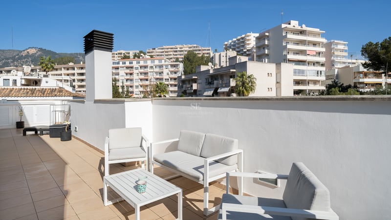 Terrasse ensoleillée avec meubles modernes blancs, carrelage et vue sur les bâtiments et les montagnes.