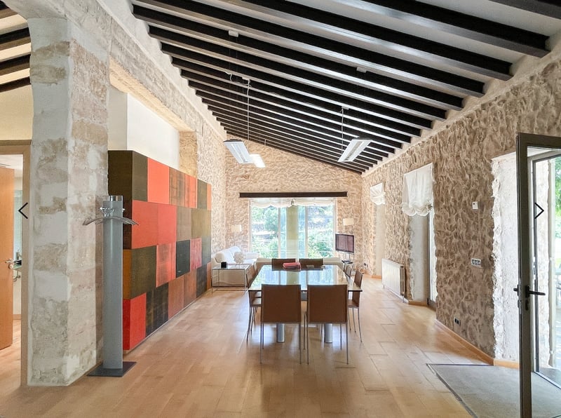 Salle à manger spacieuse avec murs en pierre, poutres en bois sombres et mobilier contemporain en verre et cuir.