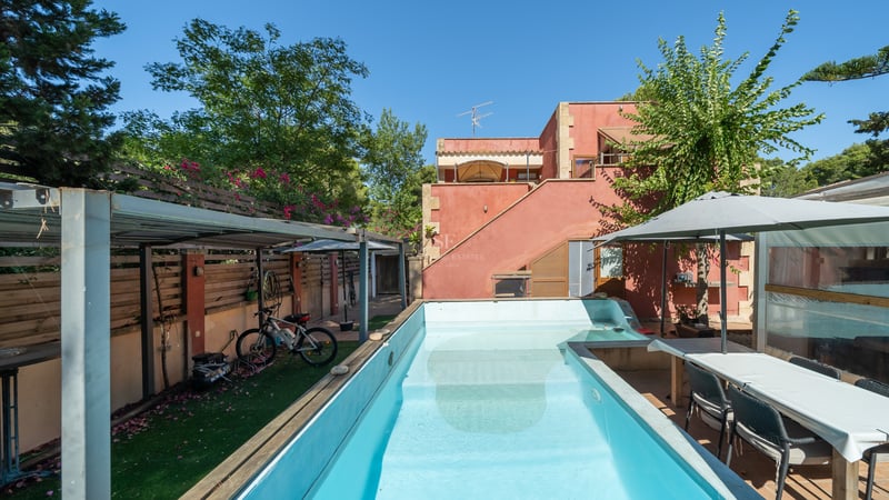 Piscine rectangulaire turquoise dans un jardin privé à côté d'une maison terre cuite avec coin repas extérieur.
