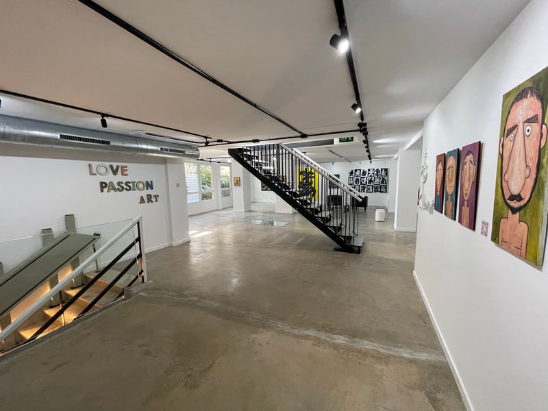 Espace industriel avec sols en béton poli, escalier en métal noir, murs blancs décorés d'art et éclairage sur rails.