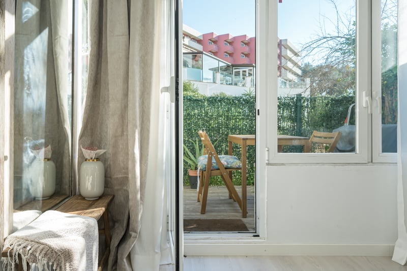 Vue à travers une porte vitrée sur une terrasse en bois avec mobilier d'extérieur et haie d'intimité.