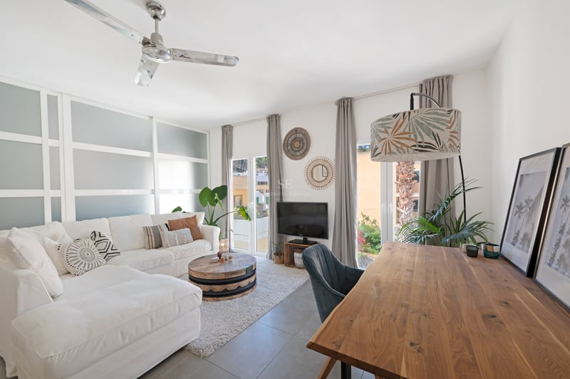 Salon moderne avec canapé blanc, bureau en bois naturel et cloison en verre dépoli ouvrant sur un balcon.