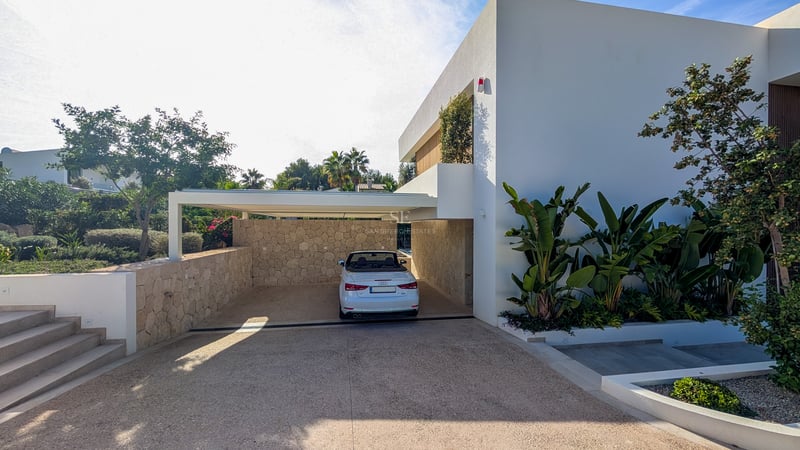 Cabriolet blanc stationné sous un abri moderne avec murs en pierre et plantes exotiques.