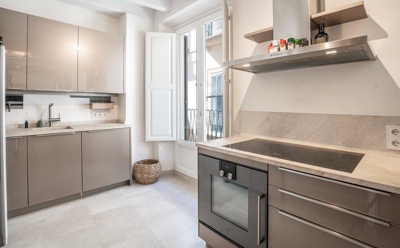 Cuisine moderne lumineuse avec placards taupe brillants, plans de travail en pierre et porte-fenêtre sur balcon.