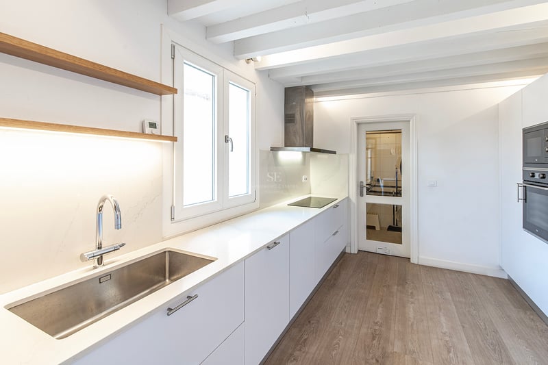 Cuisine moderne lumineuse avec placards blancs, plans de travail en quartz et poutres de plafond peintes en blanc.