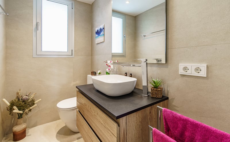 Salle de bain moderne équipée d'une vasque blanche, d'un meuble en bois, d'un grand miroir et de murs beiges.