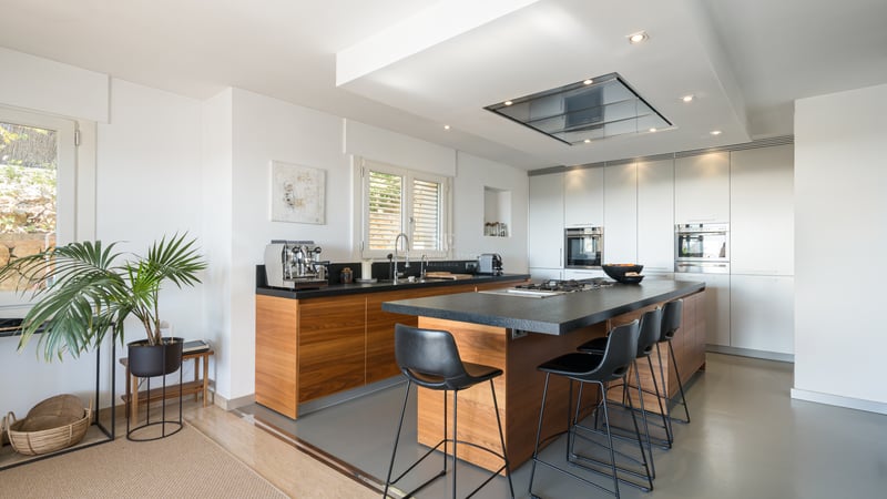 Cuisine moderne avec menuiserie en bois, îlot en granit noir avec tabourets et appareils intégrés.