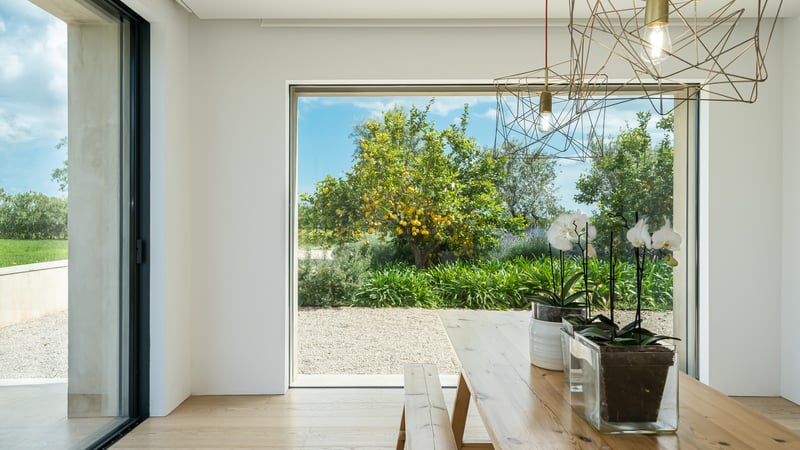 Table et banc en bois massif devant une grande baie vitrée ouvrant sur un jardin avec citronnier.
