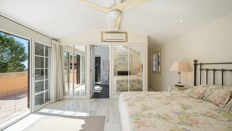 Chambre lumineuse avec sol en marbre blanc, armoires à miroirs et portes coulissantes ouvrant sur une terrasse.
