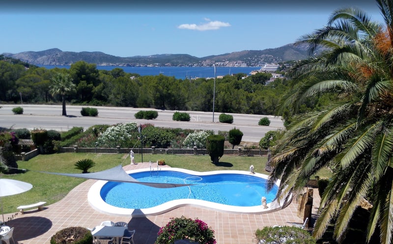 Piscine en forme de haricot entourée de terre cuite et d'un jardin avec vue sur la Méditerranée et les montagnes.