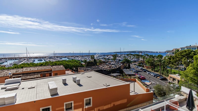 Vue surélevée surplombant un port de plaisance avec des yachts et la mer Méditerranée sous un ciel bleu clair.