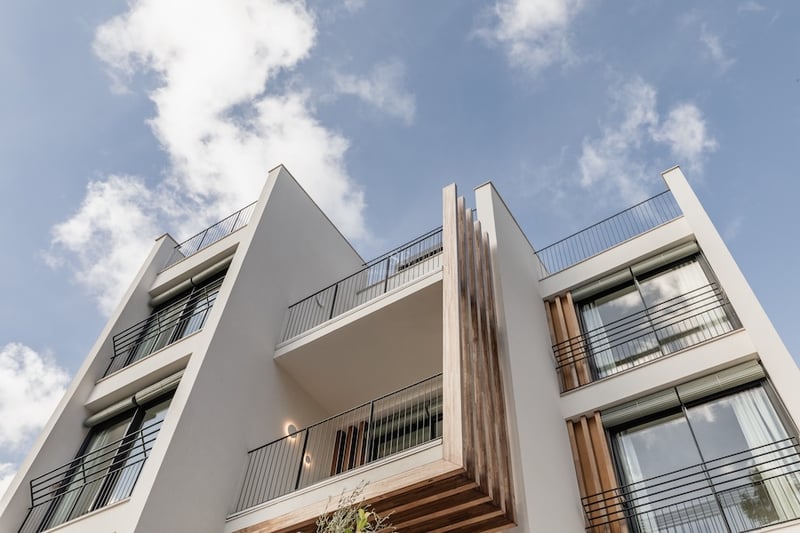Vue en contre-plongée d'une façade blanche moderne avec des accents en bois et des balustrades noires sur fond de ciel bleu.