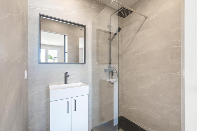 Salle de bains moderne avec carrelage gris effet pierre, paroi de douche en verre et robinetterie noire mate.