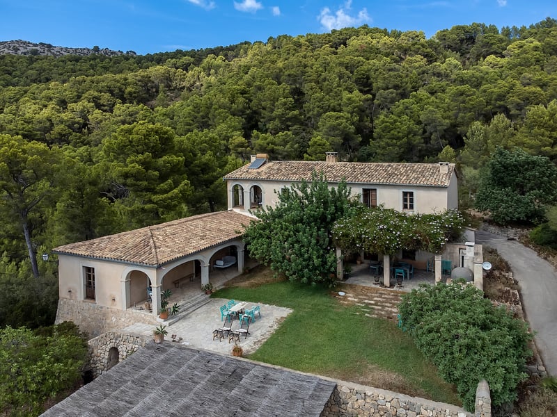 Vue surélevée d'une villa méditerranéenne en pierre avec toit en terre cuite entourée d'une forêt de pins dense.