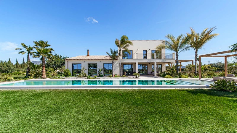 Vue extérieure d'une villa blanche moderne à deux étages avec piscine rectangulaire et pelouse sous un ciel dégagé.