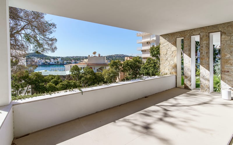 Terrasse couverte avec mur en pierre naturelle et garde-corps blanc donnant sur une baie bleue et une ville côtière.