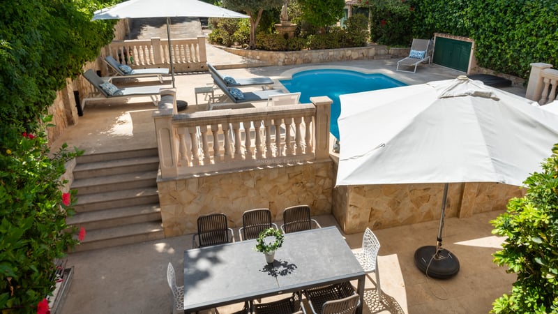 Terrasse ensoleillée sur plusieurs niveaux avec piscine, chaises longues et coin repas extérieur aux murs de pierre.