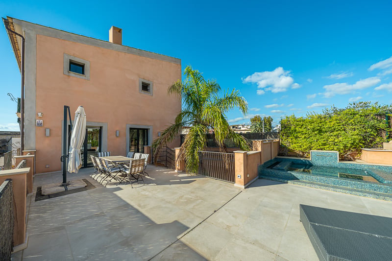 Terrasse méditerranéenne avec sol en pierre, salle à manger extérieure, palmier et petite piscine carrelée sous un ciel bleu.