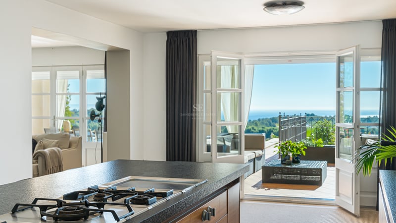 Îlot de cuisine moderne avec plan de travail en pierre noire, ouvert sur une terrasse ensoleillée avec vue sur la mer.