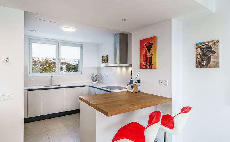 Cuisine moderne lumineuse avec placards blancs, bar en bois, tabourets rouges et électroménager en inox.