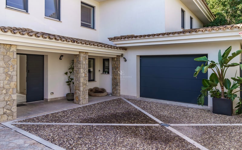 Entrée de villa moderne avec piliers en pierre naturelle, allée en galets et porte de garage gris anthracite.
