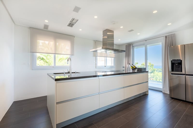 Cuisine moderne lumineuse dotée d'un grand îlot blanc avec plan de travail noir, appareils en inox et vue mer.