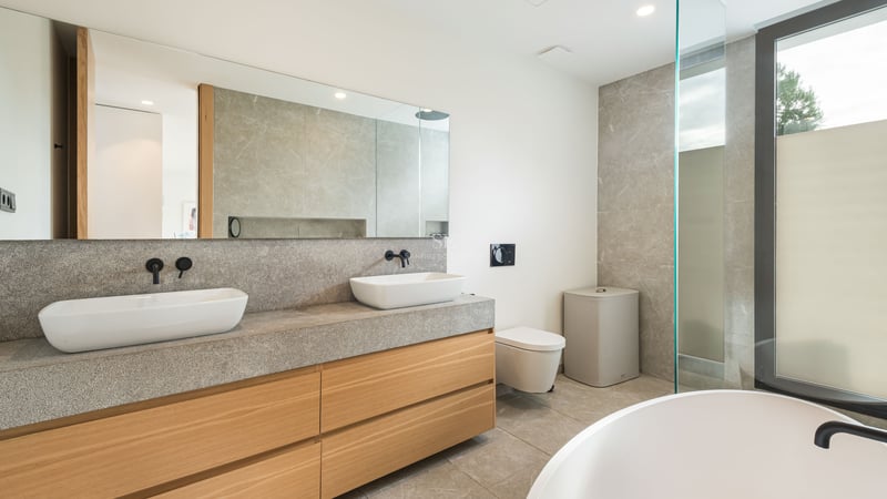 Salle de bain de luxe avec deux vasques sur un plan en pierre, meubles en bois et grand miroir.