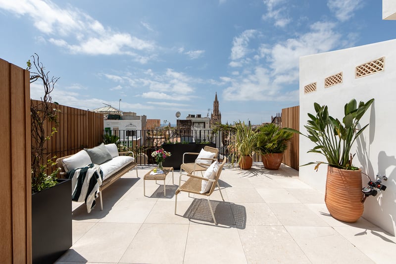 Terraza moderna en la azotea con muebles de exterior, suelo de piedra y vistas a la catedral de Palma bajo un cielo azul.
