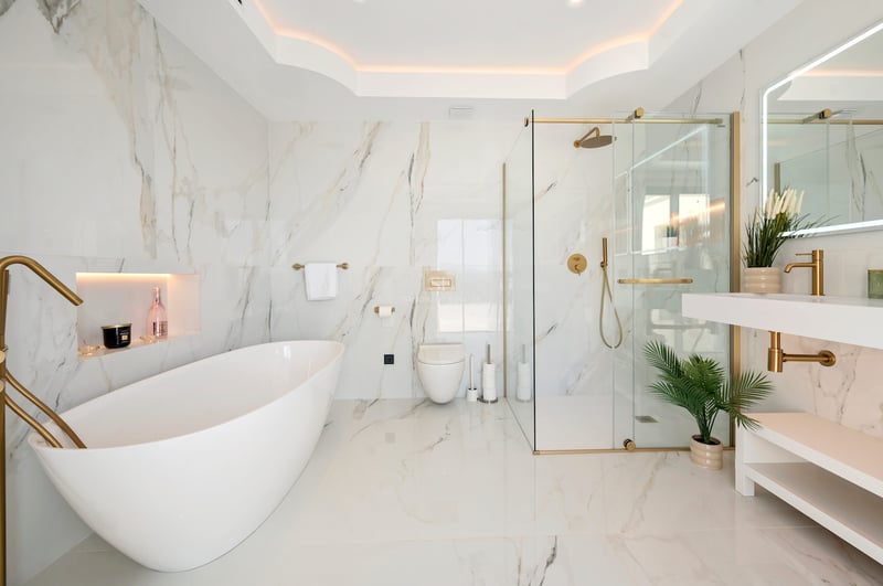 Salle de bains de luxe avec baignoire îlot, douche vitrée et robinetterie dorée sur murs en marbre.