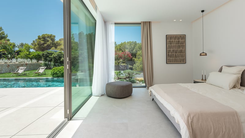 Chambre contemporaine avec baies vitrées coulissantes ouvrant sur une piscine turquoise et un jardin luxuriant.