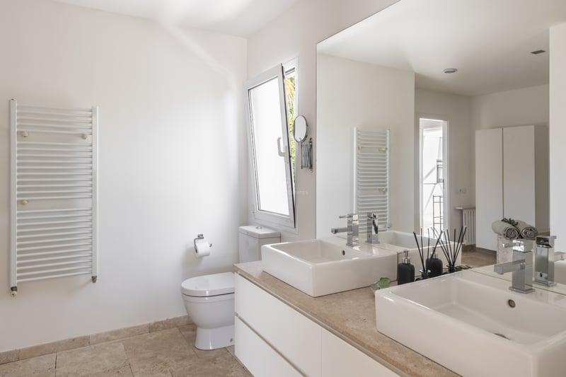 Salle de bain lumineuse avec double vasque sur plan en pierre naturelle, grand miroir et sèche-serviettes blanc.
