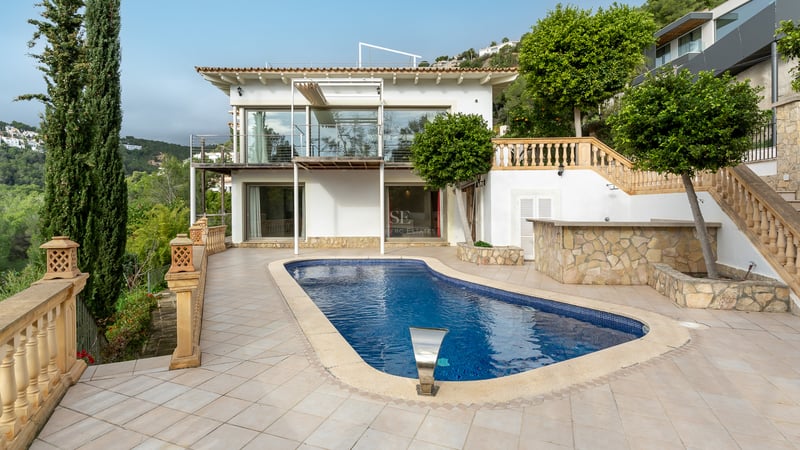 Piscine bleue sur une terrasse carrelée devant une villa blanche de style méditerranéen avec des cyprès.