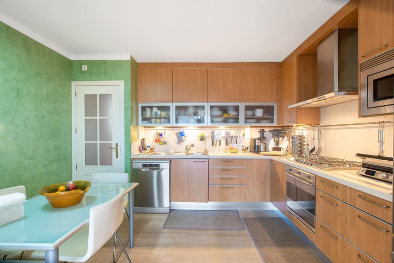 Cuisine contemporaine en bois avec appareils en inox, mur vert texturé et table de salle à manger en verre.