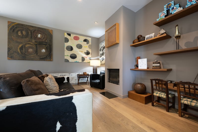 Salon moderne avec canapé en peau de vache, cheminée minimaliste, parquet en chêne et art éclectique.