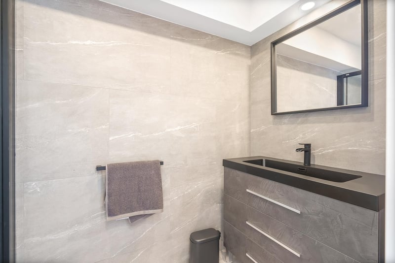 Vanité de salle de bain avec carreaux de pierre grise, vasque intégrée noire et miroir à cadre noir.