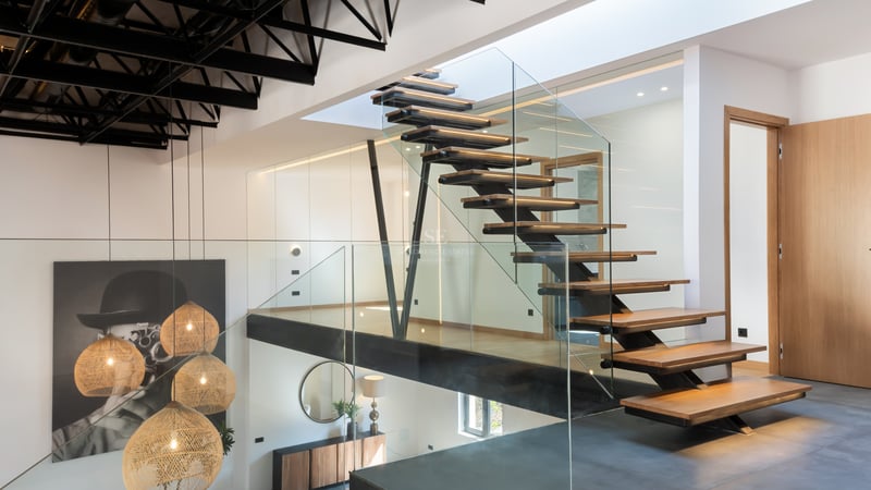 Escalier en bois et verre avec structure métallique noire et suspensions en osier dans un intérieur moderne.