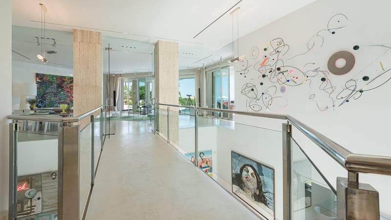 Une galerie moderne à l'étage avec des garde-corps en verre, des colonnes en travertin et de l'art contemporain.