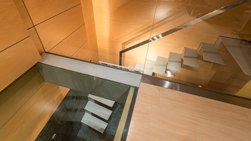 Top-down view of modern floating staircase with glass railings and warm wood wall paneling.
